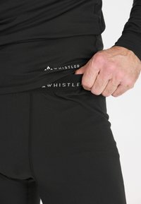 Black thermal base layer with a smooth texture. Features a logo and elastic waistband. Close-up of hand pulling the fabric.