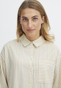 Striped button-up shirt in cream and tan, featuring a classic collar, chest pocket with matching stripes, and a relaxed fit.