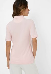 Kortærmet polo skjorte i blød pink stof med en foldet krave og sideåbninger. Glat tekstur, afslappet design, uden synlige logoer eller mønstre.