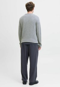 Pull en tricot gris avec un col rond, associé à un pantalon ample gris foncé. La tenue présente des bords côtelés et une texture douce.