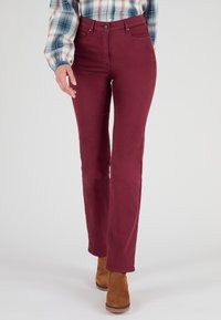 Jeans acampanados color burdeos con una cintura alta, fabricados en algodón, que cuentan con cinco bolsillos y un cierre de cremallera en la parte delantera, combinados con botas altas marrones.