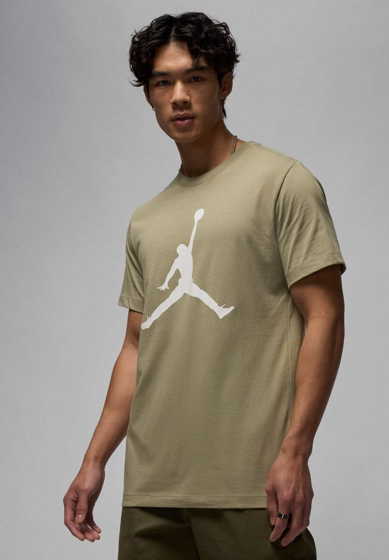 T-shirt w kolorze oliwkowej zieleni z dużym białym nadrukiem logo Air Jordan na środku. Krótkie rękawy i okrągły dekolt.