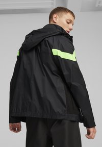 Zwarte waterdichte jas met een capuchon, voorzien van neon groene horizontale strepen op de schouders, mesh details en een relaxte pasvorm.