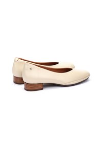 Bailarinas de piel beige con un bajo tacón de madera. Punta redondeada y un acabado suave, con un pequeño acento metálico en la parte trasera.