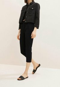 Veste cropped en denim noir, haut noir, pantalon noir ajusté et sandales noires à glissière. Textures lisses, design minimaliste.