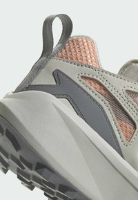 Ljust grå sportskor med meshdetaljer i rosa och grå accenter. Tjock gummisula med texturerat mönster för grepp. Ögla vid hälen för enkel påtagning.