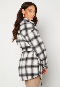 Schwarz-weiß kariertes Button-up-Shirt mit langen Ärmeln, einem Taillengürtel und einem abgerundeten Saum. Hergestellt aus einem weichen, strukturierten Stoff.