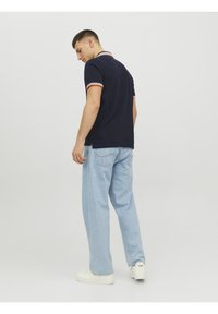 Marineblå polo skjorte med rød og hvid kant, parret med lyseblå, løstsiddende jeans og hvide sneakers, set fra ryggen.
