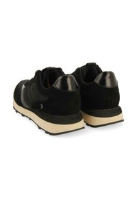 Zapatillas negras con materiales de ante y malla, que presentan un tacón negro brillante y una suela de goma beige. Diseño clásico con acentos mínimos.