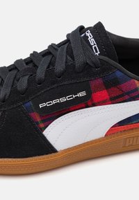 Svart mocka sneakers med ett rutigt mönster i röd, blå och gul, vita läderdetaljer och sula av gummi. Har svarta snören och branding.