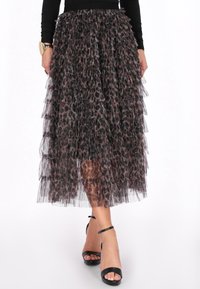 Leopardprint tulle nederdel med lagdelte flæser, midt på læggen, med en sort talje. Modellen har strappy sorte hæle på.