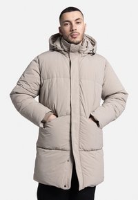 Jachetă bej captusită cu glugă, fermoar frontal și buzunare laterale. Prezintă un design matlasat și manșete elastice pentru căldură.