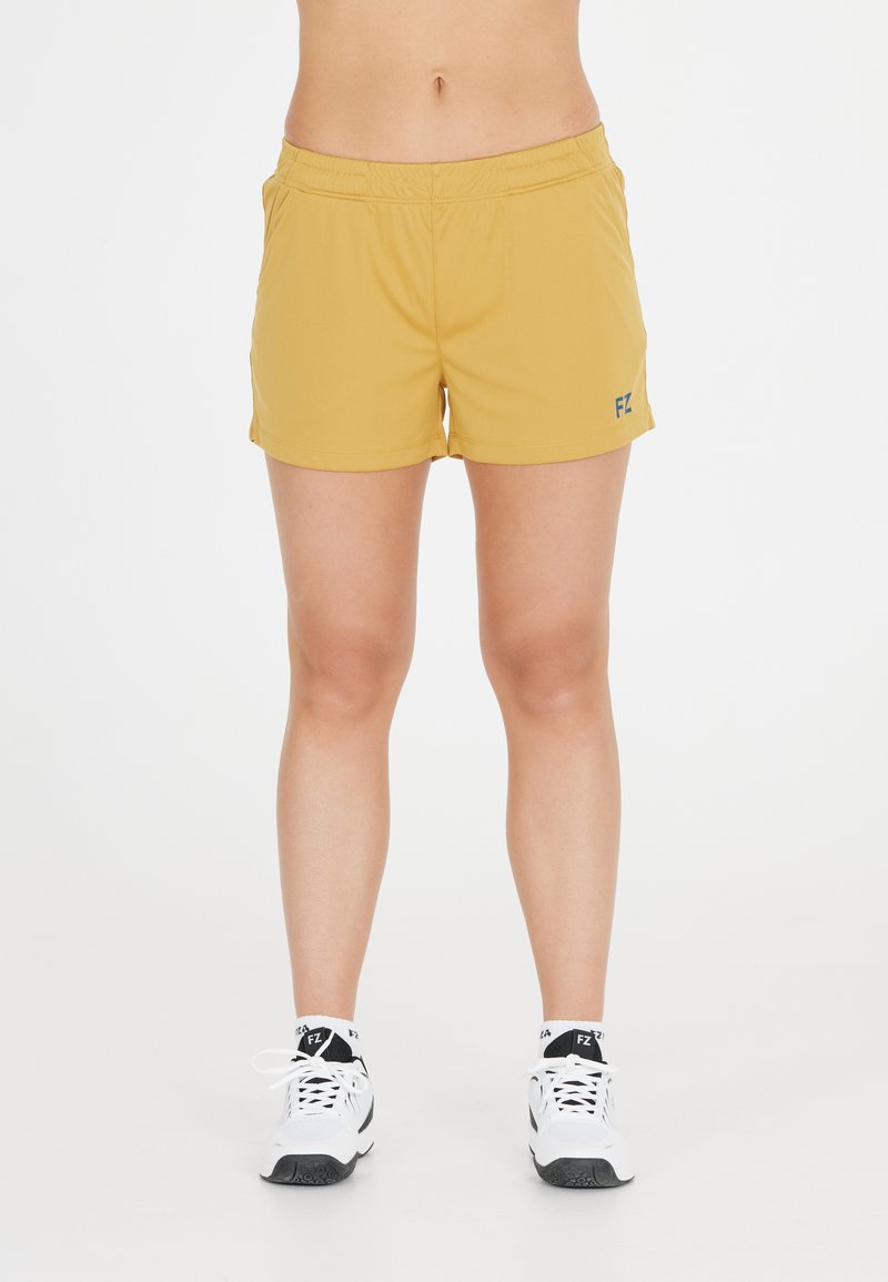 Gula sportshorts med resårmidja. Har en blå logo på vänster sida. Bärs med vita sportskor.
