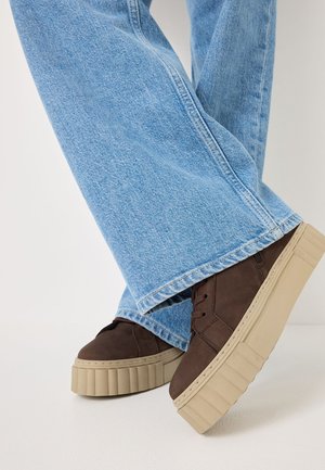 Des chaussures à plateforme en daim marron avec une semelle en caoutchouc beige texturé, assorties à un jean léger à jambe large bleu clair, mettant en avant un style décontracté.