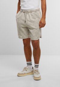 Shorts de sport gris avec un motif texturé, une taille élastique et des fentes sur les côtés. Associés à des baskets blanches et beiges et des chaussettes rayées.