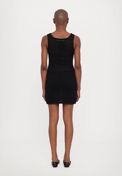 Rochie neagră fără mâneci, cu un design ajustat, având un model texturat din tricot și o margine deasupra genunchiului. Textură netedă, accente minime.