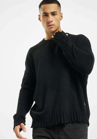 Sweater noir tricoté à la coupe ample, avec un col rond et des poignets effilés. Tissu texturé avec des détails d'ourlet flottants.