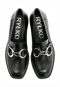 Czarne skórzane mokasyny z kwadratowym noskiem, ozdobione podwójnym srebrnym pierścieniem oraz teksturowaną podeszwą. Na wkładce widnieje napis "RYŁKO".