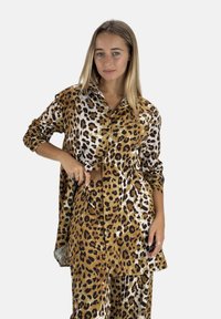 Conjunto de camisa y pantalones con estampado de leopardo, que presenta colores marrón, beige y negro. Hecho de tela suave con un ajuste relajado y detalles de botones.