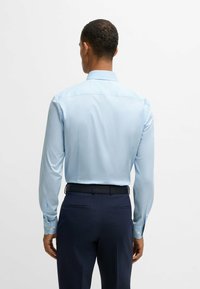 Hellblaues, langärmliges Hemd mit glatter Textur und traditionellem Kragen. Trägt es mit dunkelblauen Hosen.