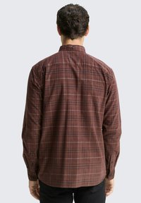 Chemise à manches longues marron à carreaux avec un col boutonné, présentant des rayures plus claires discrètes et des poignets à bouton, vue de dos.