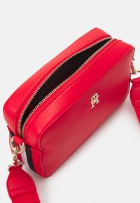 Punainen suorakulmainen olkalaukku, joka on valmistettu teksturoidusta nahasta ja varustettu kaksoissalaisella vetoketjulla, kultaisilla yksityiskohdilla ja säädettävällä hihnalla.