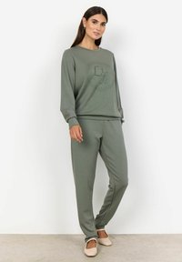 Olijfgroen loungewear-set met een langwerpig shirt met een circulaire grafiek en bijpassende tapered broek, gemaakt van zachte, lichtgewicht stof.