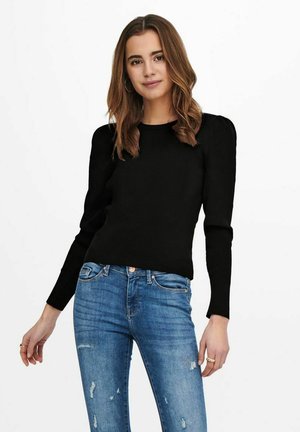 Top lungo a maniche rigate nere con spalle a sbuffo, abbinato a jeans blu medio strappati. Scollo rotondo semplice e design aderente.