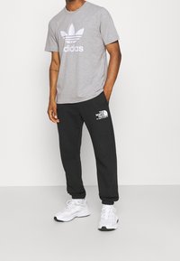 Šedé bavlněné tričko s bílým logem Adidas, doplněné černými tepláky s bílým logem The North Face a bílými teniskami.