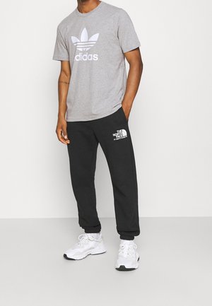 Grå bomullst-shirt med vitt Adidas-logotyp, kombinerad med svarta sweatpants med vitt North Face-logotyp, kompletterade med vita sneakers.