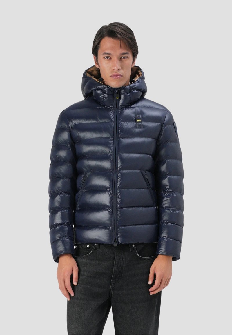 Giubbino trapuntato blu navy con finitura lucida, chiusura con zip, cappuccio attaccato e imbottitura in piuma. Presenta un motivo trapuntato e dettagli con logo.