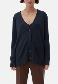 Granatowy kardigan z dekoltem w serek, z przodem zapinanym na guziki, żebrowanymi detalami i luźnym krojem. Wykonany z miękkiego dzianinowego materiału.