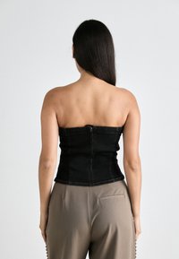 Μαύρη τζιν strapless τοπ με εφαρμοστή σχεδίαση, κάθετες ραφές και κλείσιμο με φερμουάρ στην πλάτη. Φοριέται με ανοιχτόχρωμες ψηλόμεσες παντελόνες.