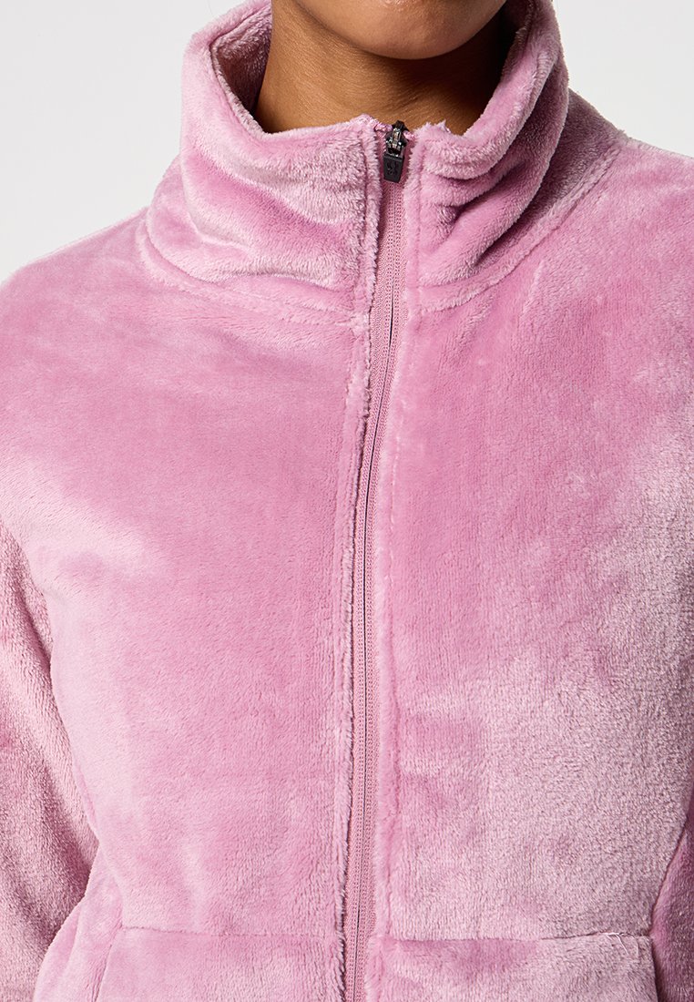 Różowa polarowa kurtka z wysokim kołnierzem, z zamkiem błyskawicznym z przodu i miękką, fakturowaną powierzchnią. Brak widocznych wzorów lub dodatkowych detali.