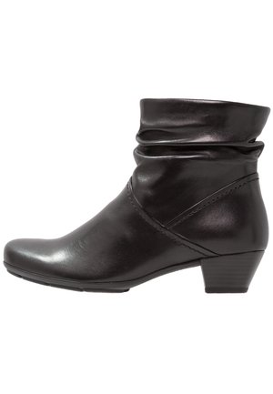 Bottine en cuir noir avec un petit talon empilé et un design supérieur légèrement tombant sur fond blanc.