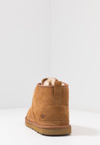 Stivale alla caviglia in suede marrone con una morbida fodera, suola in gomma piatta e linguetta sul retro, caratterizzato da un discreto dettaglio del logo sul lato.