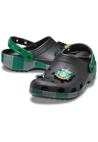 Schwarze Holzschuhe mit einem grün-grauen gestreiften Band, das ein Slytherin-Emblem und Belüftungsöffnungen aufweist. Verstellbarer Fersenriemen für sicheren Sitz.