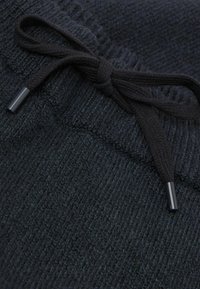 Czarna dzianina z bliska, związaną troczkiem z gładkimi czarnymi końcówkami, ukazująca teksturowaną, miękką powierzchnię i subtelny wzór splotu.