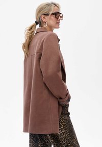 Bruine oversized blazer met een zachte textuur, lange mouwen en een subtiele achterste schoudernaad, gecombineerd met panterprintbroek.