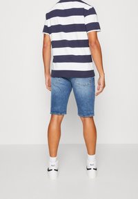 Camisa de manga corta a rayas en azul marino y blanco para hombres, combinada con pantalones cortos de mezclilla azules y zapatillas blancas con detalles en negro. Ajuste casual y relajado.
