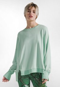 Mintunvihreä pitkähihainen collegepaita rentoutuneella istuvuudella, pudotetyt olkapäät, sivuhalkiot ja resorinen pääntie. Pehmeä kangas, jossa sileä pinta.