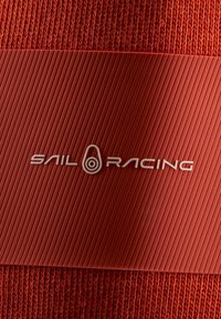 Tissu rouge texturé avec un bandeau en caoutchouc côtelé rouge affichant le logo "Sail Racing" en blanc au centre.