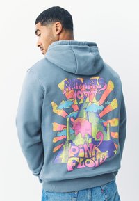 Pilkas džemperis su gobtuvu, ant nugaros spalvingas grafinis dizainas su kiaule, debesimis ir užrašu „Animals 1977 Pink Floyd“ ryškiomis spalvomis.