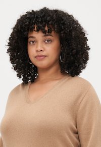Pull beige en tricot doux avec décolleté en V, présentant un col côtelé et des manches longues, avec une coupe décontractée et une texture lisse.