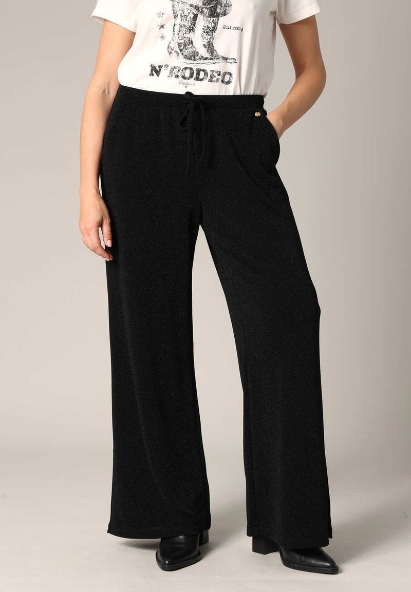 Zwarte wijde broek gemaakt van een zachte, textuurstof. Voorzien van een elastische tailleband met een trekkkoord en zijzakken.