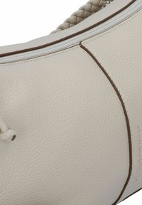 Bolso de mano de cuero beige con superficie texturizada, que presenta costuras marrones y una correa trenzada, cierre de cremallera y un diseño minimalista.