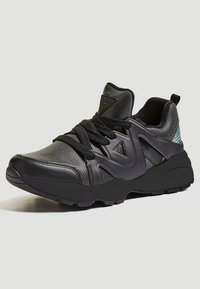 Sneaker atletico nero con una tomaia in mesh testurizzato, accenti in sintetico liscio, suola spessa e un sistema di allacciatura prominente per una vestibilità sicura.