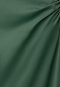Grön tyg med en jämn textur, som har mjuk drapering och subtil lyster. Materialet verkar lätt och elastiskt.