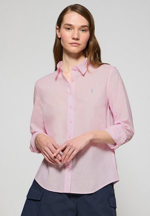 Camicia button-up rosa chiaro con colletto, patta frontale trasparente e maniche arrotolate. Presenta un piccolo logo blu sul lato sinistro del petto.