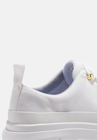 Baskets blanches en toile avec une finition texturée, un bout arrondi, des détails cousus et un petit logo. Comprend un œillet doré et une languette en boucle.